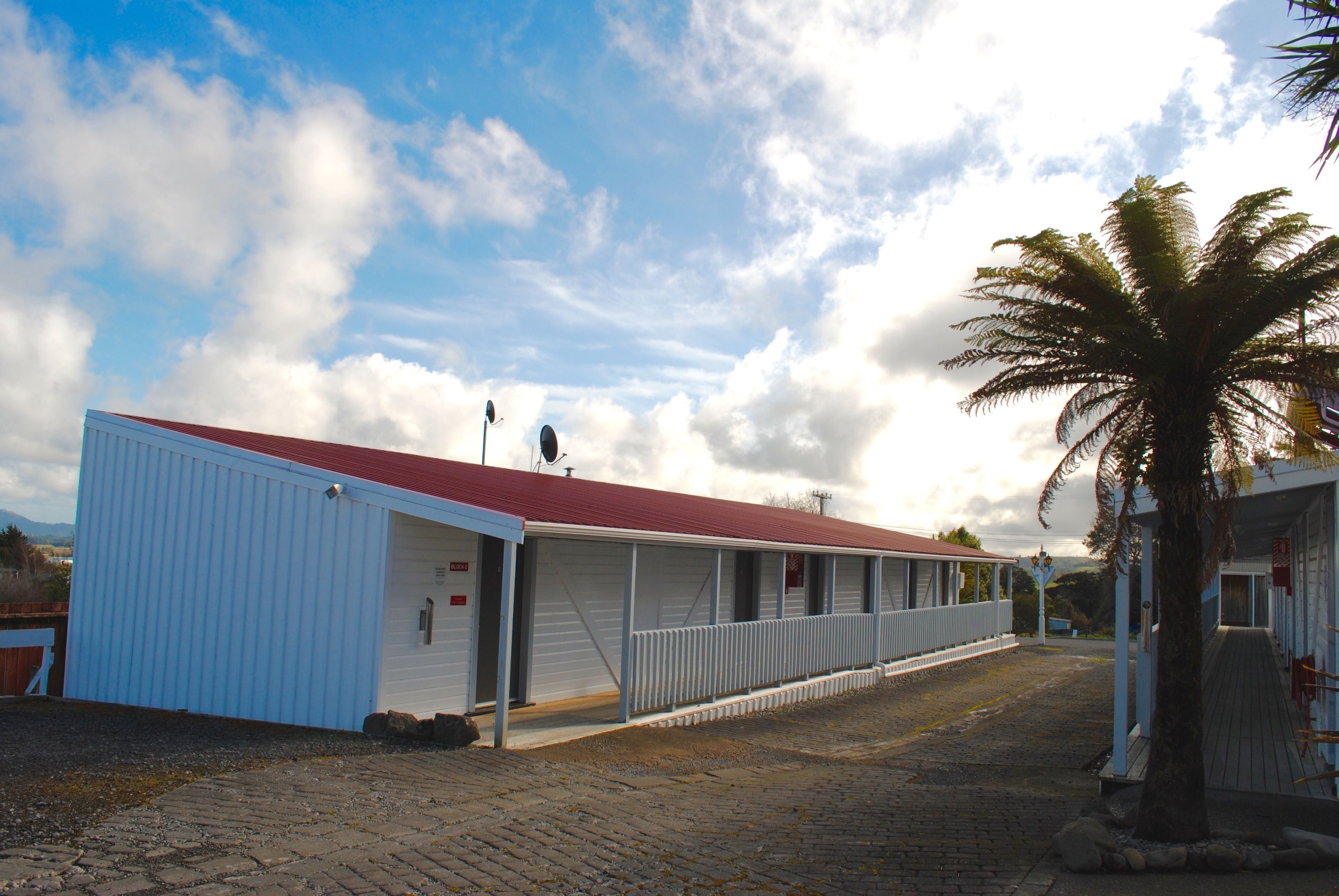 Een rij gelijkvloerse gebouwen met een rood dak, een overdekte gangpad en een palmboom.