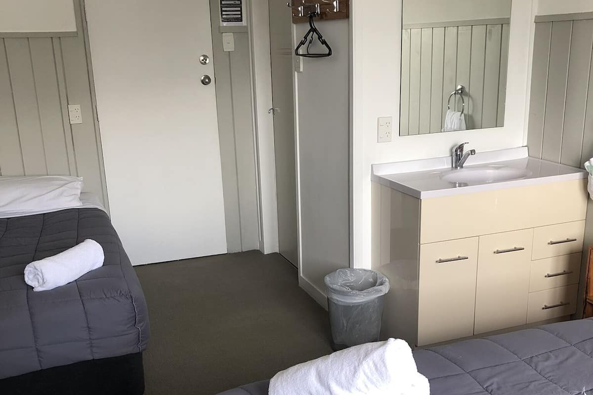 A hotel room with two beds, a bathroom with a sink and mirror, and a door with a sign.