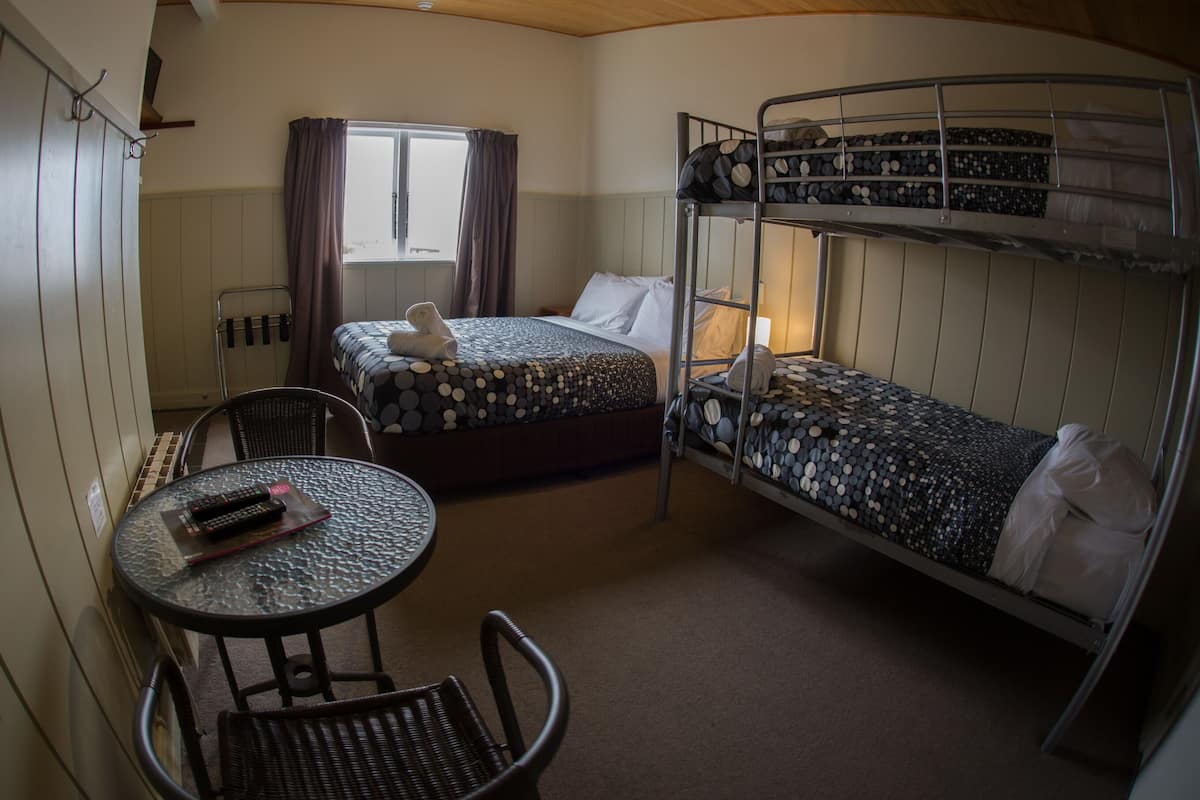 A bunk bed room with a round table and chairs, a window with curtains, and a bed with a polka dot blanket.