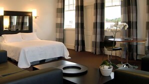 A hotel room with a bed, a sofa, a small table with a vase of flowers, and a view of the outdoors through the window. - The White Swan Country Hotel (Greytown)