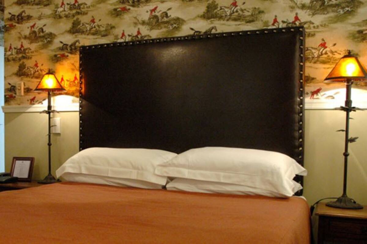 A hotel room with a large bed, two bedside lamps, a wooden chair, and a desk.