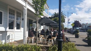 An outdoor seating area with tables and chairs, a covered section with umbrellas, and a street view with cars and a flag. - The White Swan Country Hotel (Greytown)