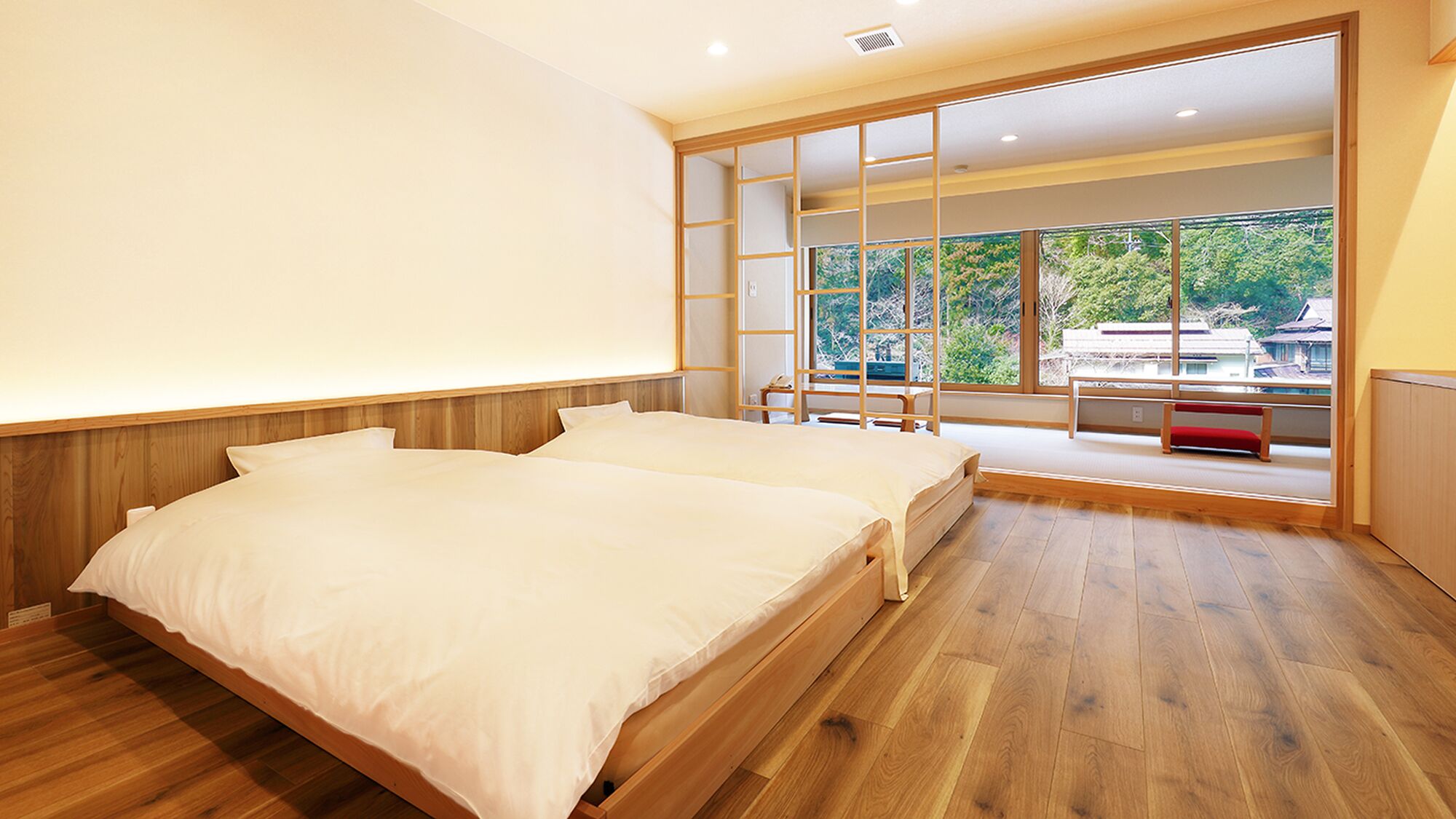 A bedroom with two beds, a sliding glass door leading to a balcony, and a view of greenery outside.