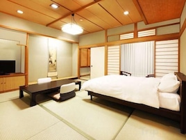 Un dormitorio de estilo japonés tradicional con suelo de tatami, una cama, un escritorio y un televisor.