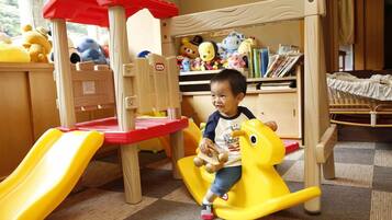 A child playing on a yellow and red play structure with a slide, surrounded by toys and bookshelves.