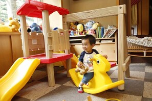 A child playing on a yellow and red play structure with a slide, surrounded by toys and bookshelves. - Ryokan Yubara International Tourist HOT (MANIWA SHI)