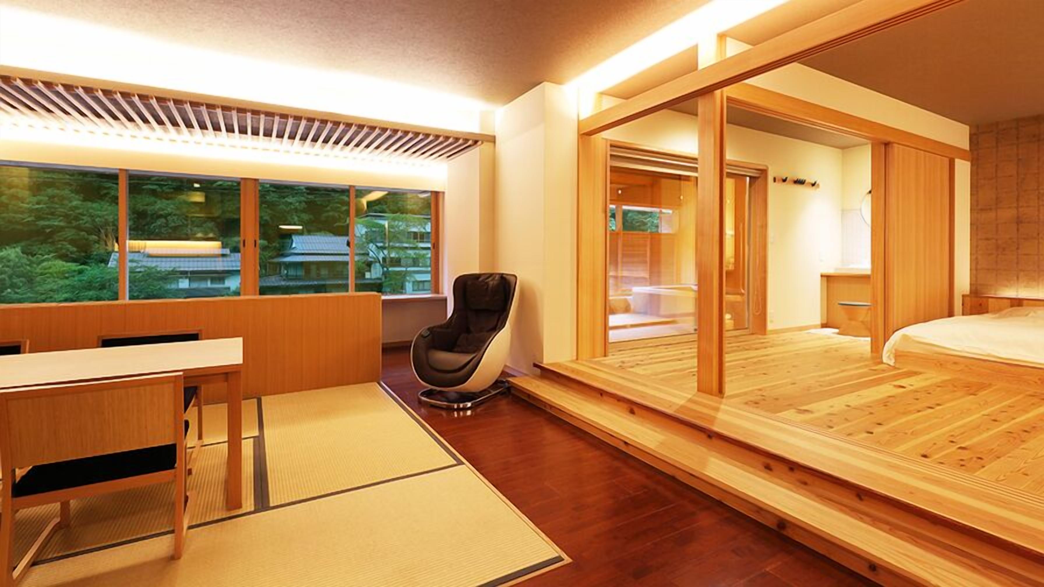 A modern hotel room with a wooden floor, a desk with a chair, a large bed, and a sliding door leading to a bathroom.