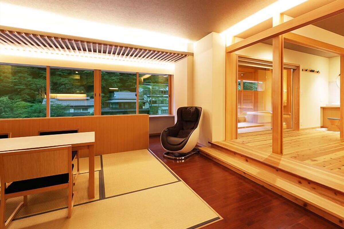A modern hotel room with a wooden floor, a desk with a chair, a large bed, and a sliding door leading to a bathroom.
