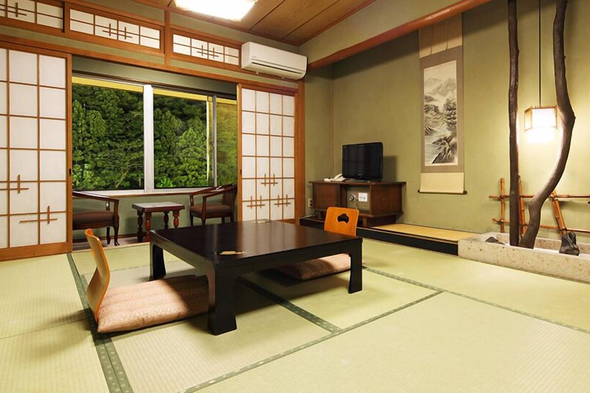 A traditional Japanese room with tatami flooring, a low table, chairs, a television, and a sliding door.