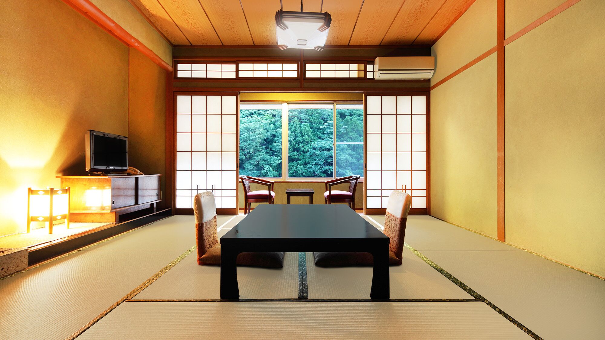 A traditional Japanese room with tatami flooring, a low table, and a television on a cabinet.
