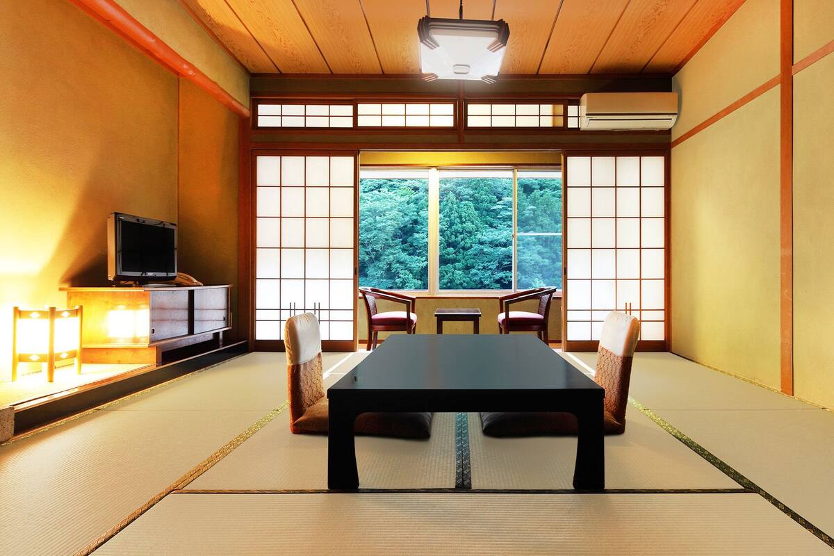A traditional Japanese room with tatami flooring, a low table, and a television on a cabinet.
