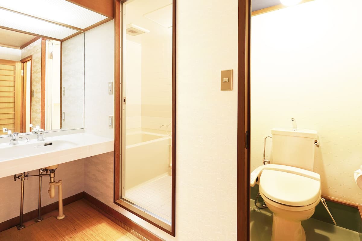A bathroom with a large mirror, a sink, a toilet, and a shower area.