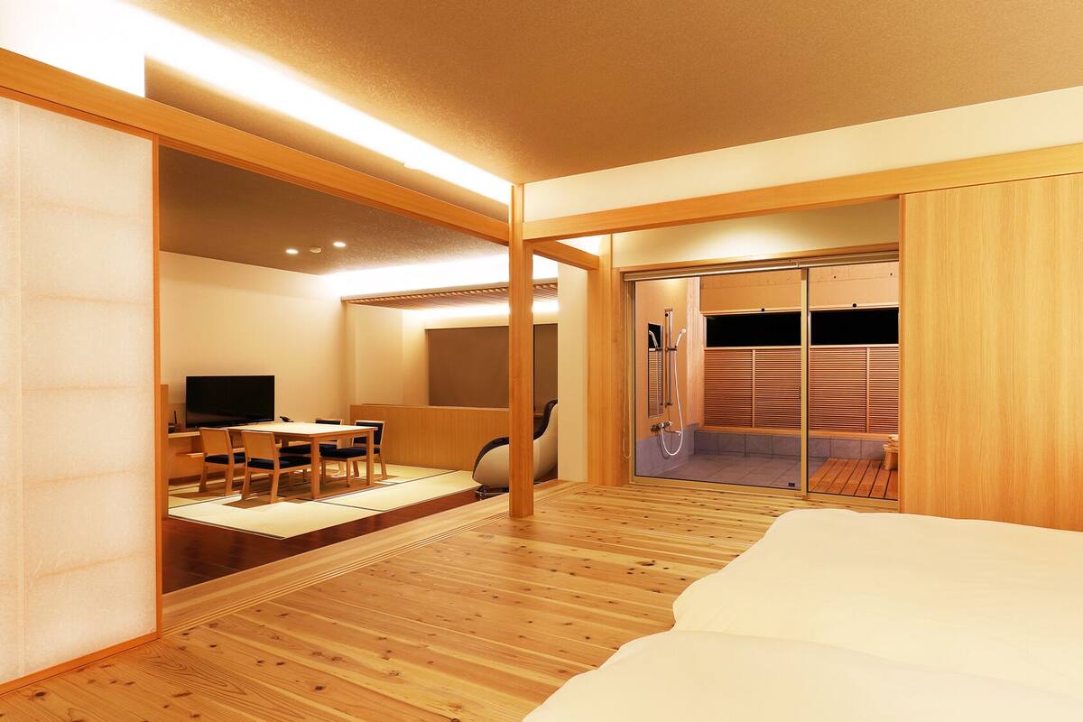 A modern hotel room with a wooden floor, a bed, a TV, a desk, and a sliding door leading to a shower area.