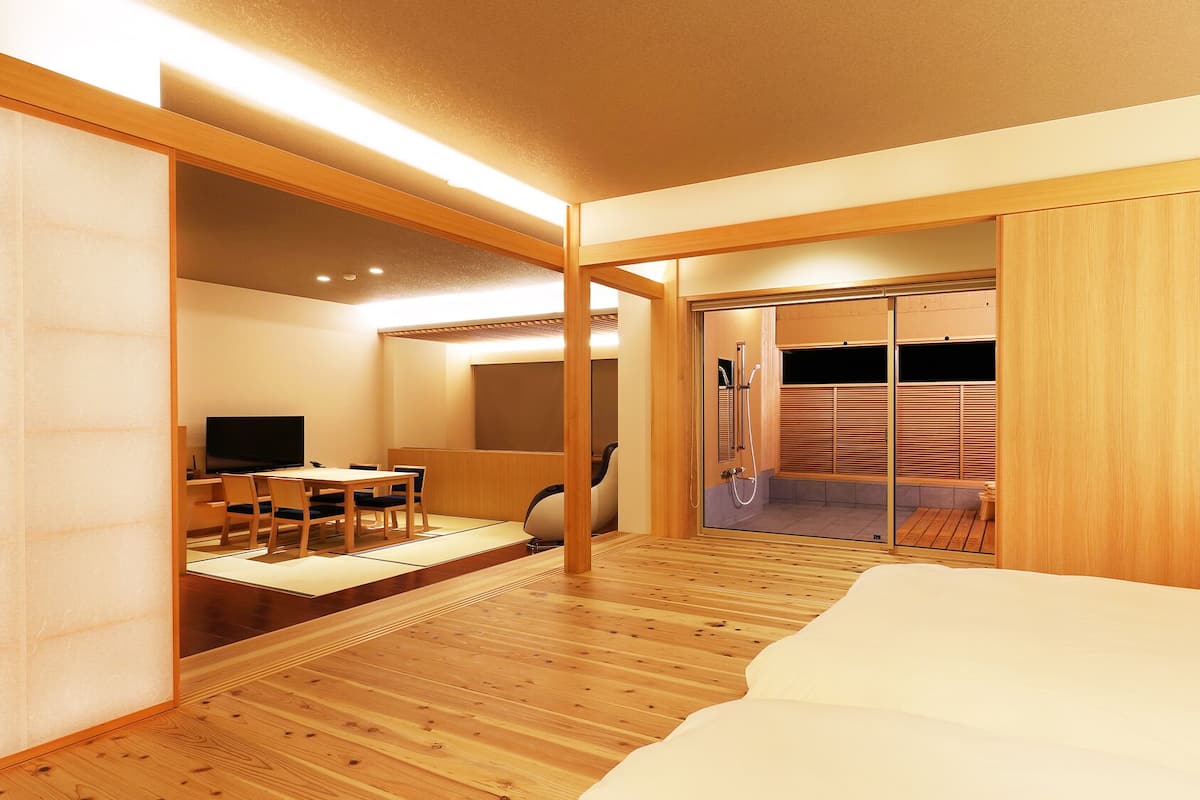 A modern hotel room with a wooden floor, a bed, a TV, a desk, and a sliding door leading to a shower area.