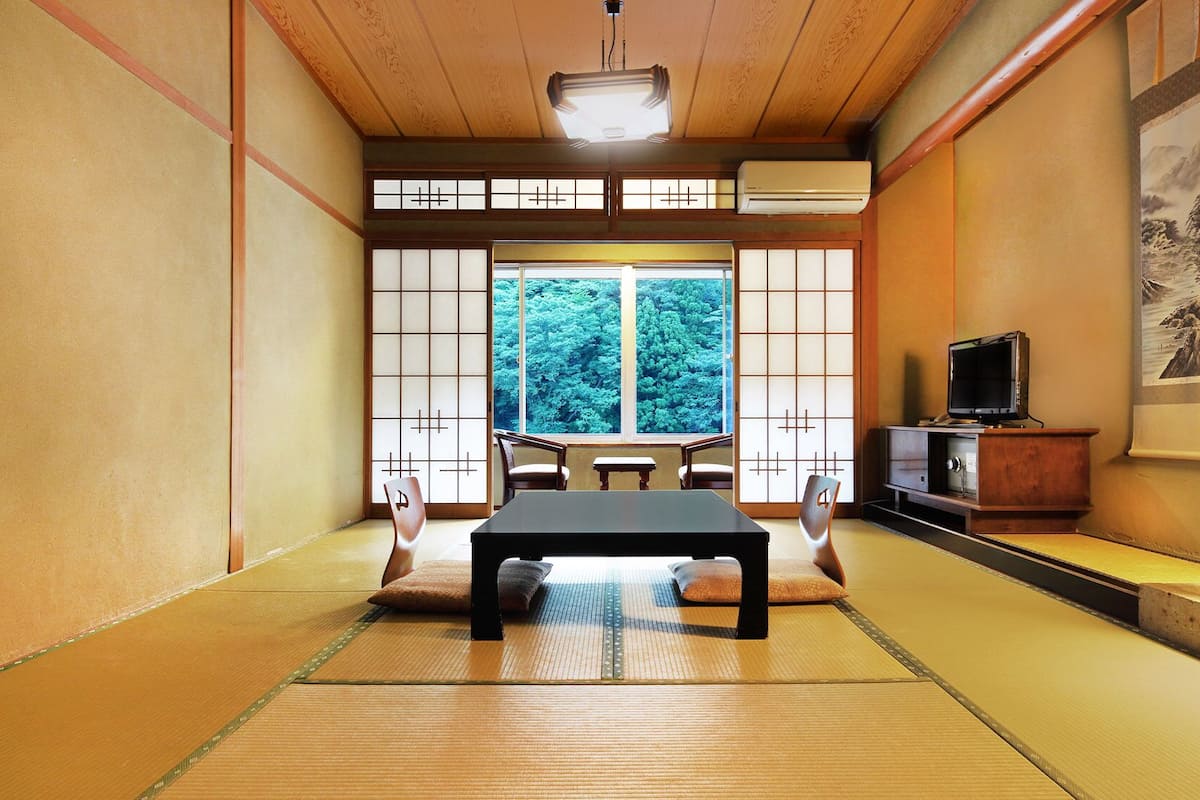 A tatami mat room with a futon bed, sliding shoji doors, a television, and a painting on the wall.