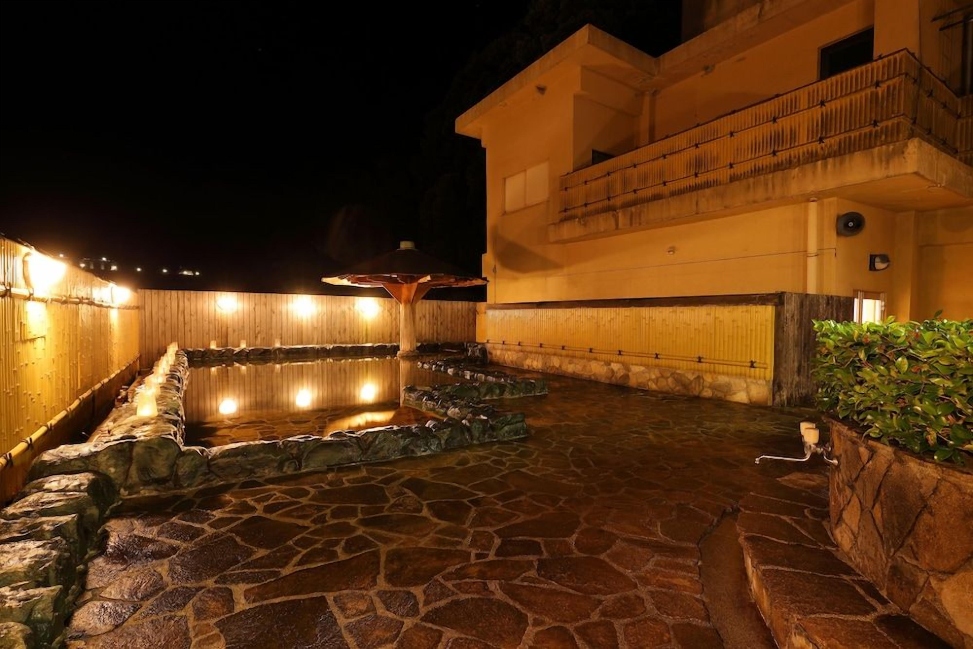 A stone-floored outdoor area with a pool, surrounded by walls and a building with a balcony.