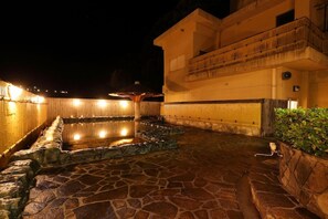 A stone-floored outdoor area with a pool, surrounded by walls and a building with a balcony. - Ryokan Yubara International Tourist HOT (MANIWA SHI)