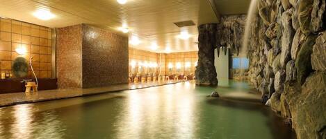 An indoor swimming pool with a stone wall on one side and a wooden ceiling.
