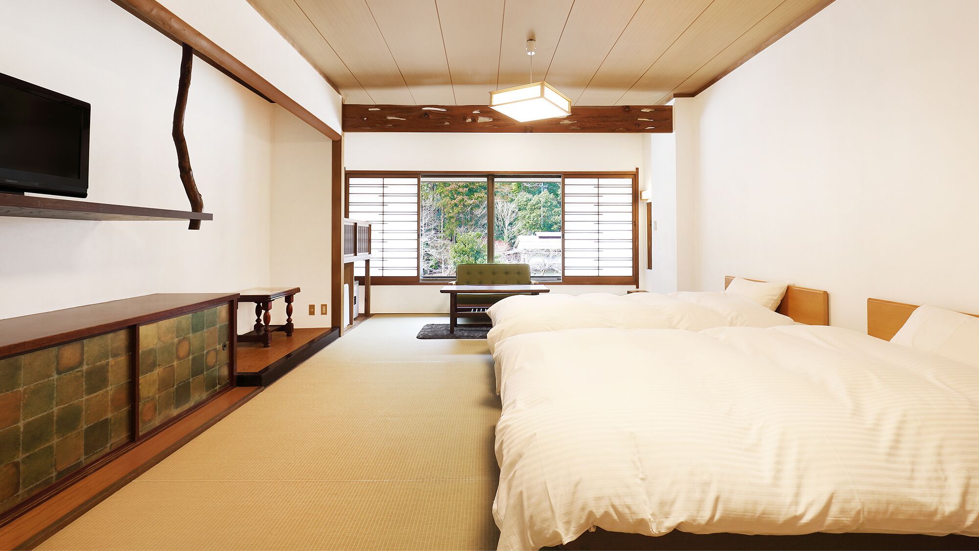 A hotel room with a bed, a TV, a desk, and a view of trees through the window.