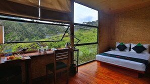 Un dormitorio con un ventanal grande, una cama, un escritorio con silla y vistas a zonas verdes.
