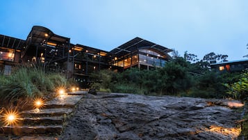 Un bâtiment moderne à plusieurs étages, doté de grandes fenêtres et entouré d’une végétation luxuriante.