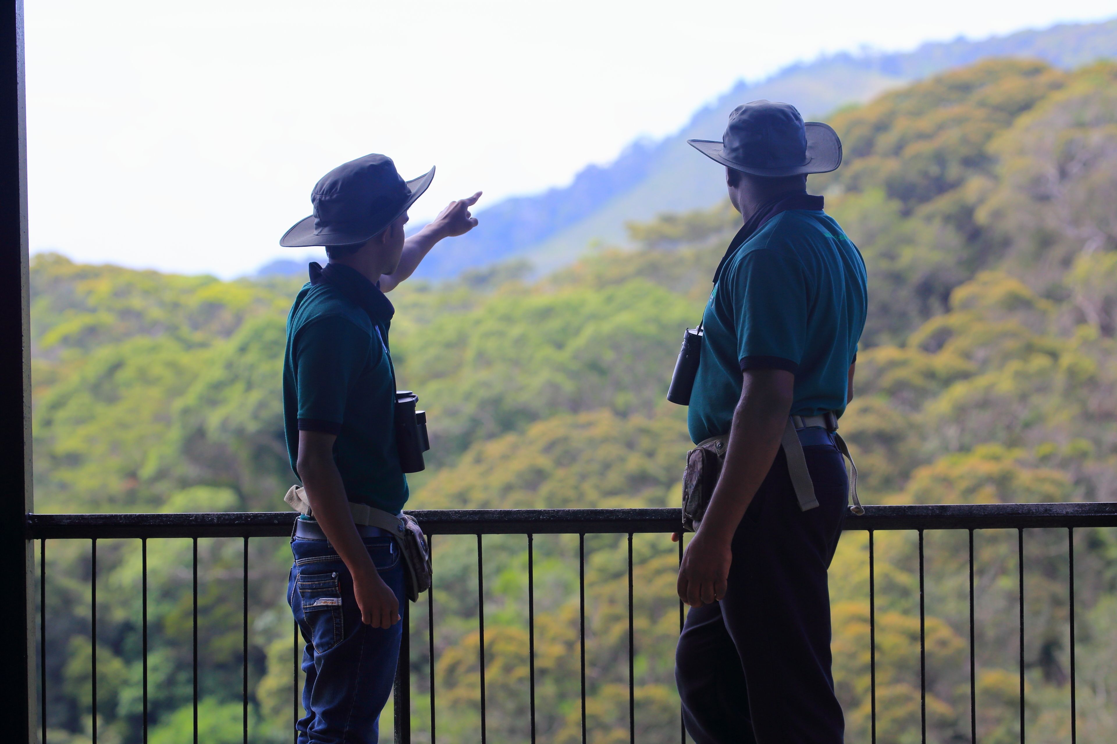 Dos personas junto a una barandilla, con vista a un paisaje montañoso.