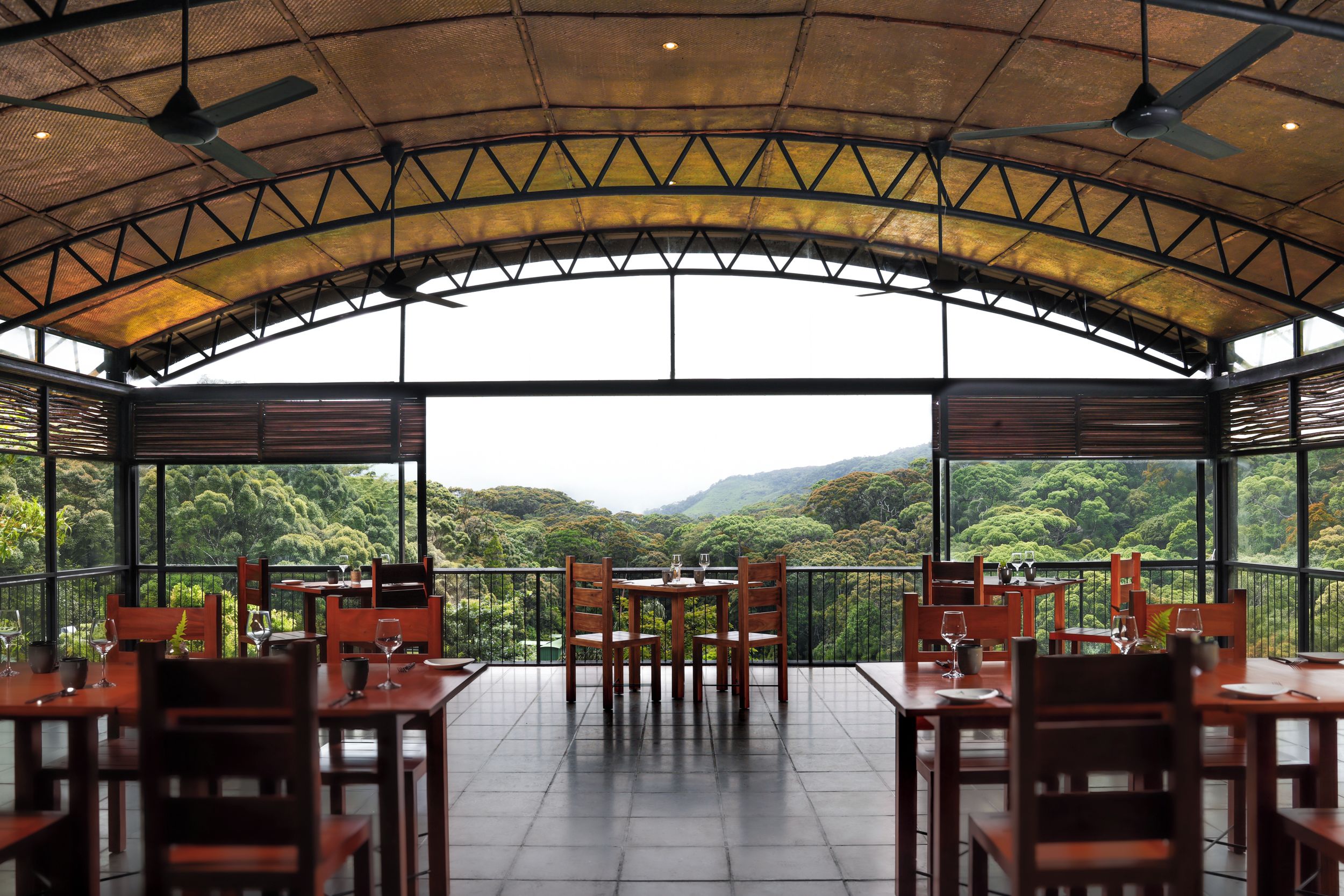 An outdoor dining area with tables and chairs, large windows offering a view of a forested landscape.