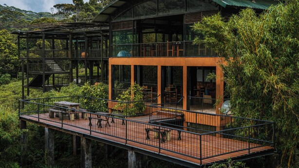 Un edificio moderno con varios niveles, mesas al aire libre y una terraza de madera.