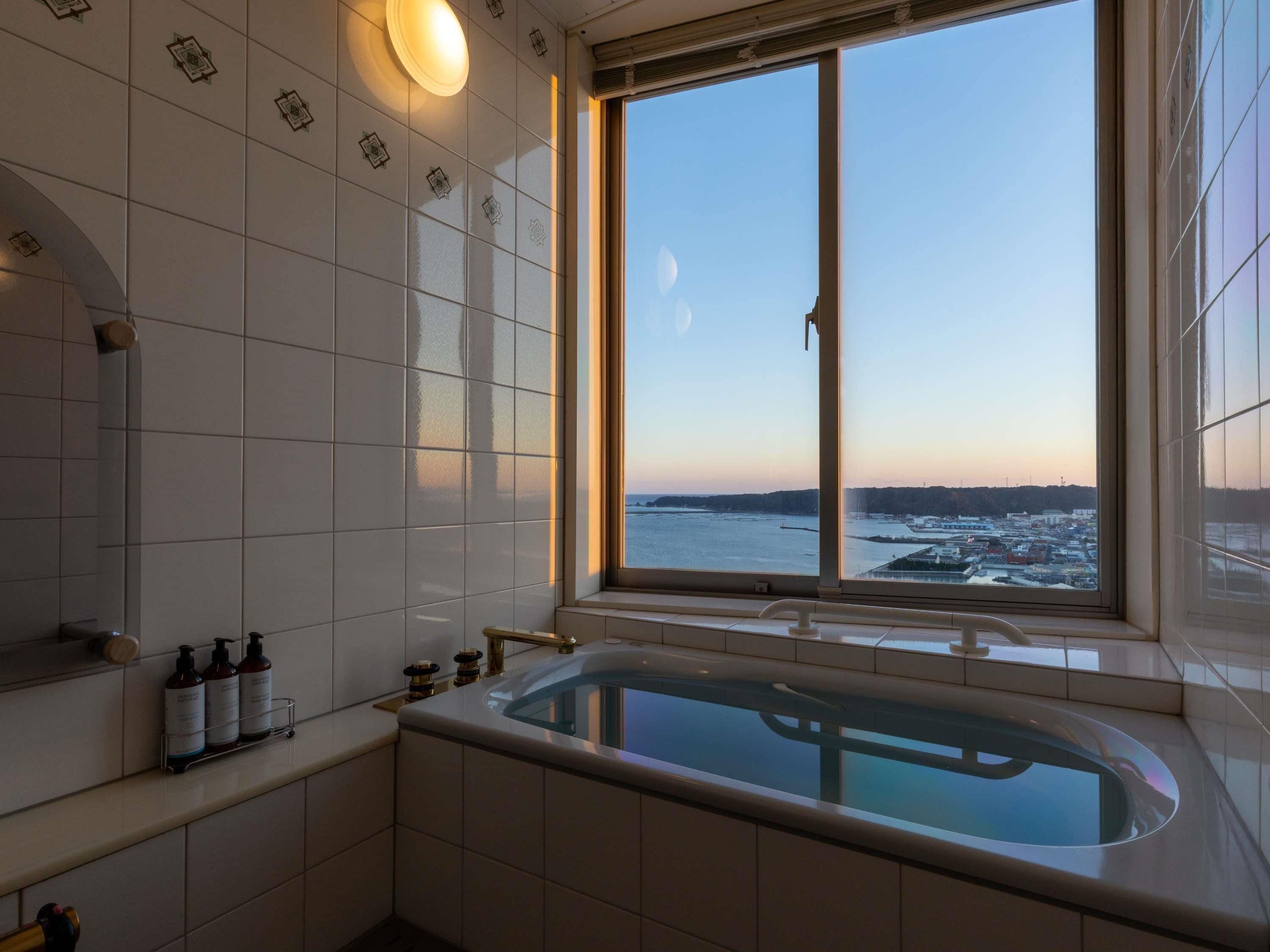 Un baño moderno con una bañera grande, una ventana con vistas a una masa de agua y un estante con artículos de aseo.