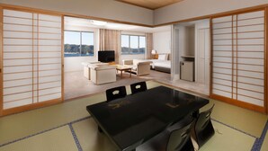 Habitación de hotel con suelo de tatami, una mesa de comedor, televisión, cama y vista al mar.