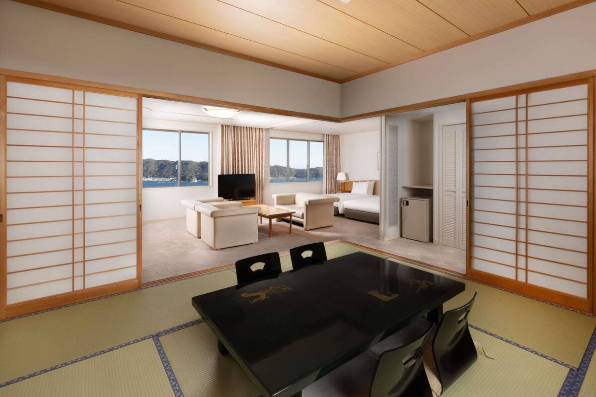 Ein Hotelzimmer mit Tatami-Bodenbelag, einem Esstisch, einem Fernseher, einem Bett und Meerblick.