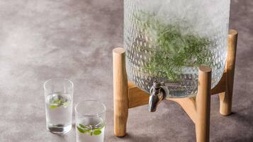 Un recipiente di vetro trasparente con ghiaccio e foglie di menta, un rubinetto metallico e due bicchieri con acqua e foglie di menta.