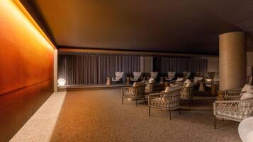 A dimly lit lounge area with wicker chairs and a large pillar, carpeted floor, and a curtain wall in the background.
