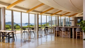 Amplio espacio interior con grandes ventanales que ofrecen vistas a un puente y zonas verdes. Hay mesas y sillas dispuestas para comer o reuniones.