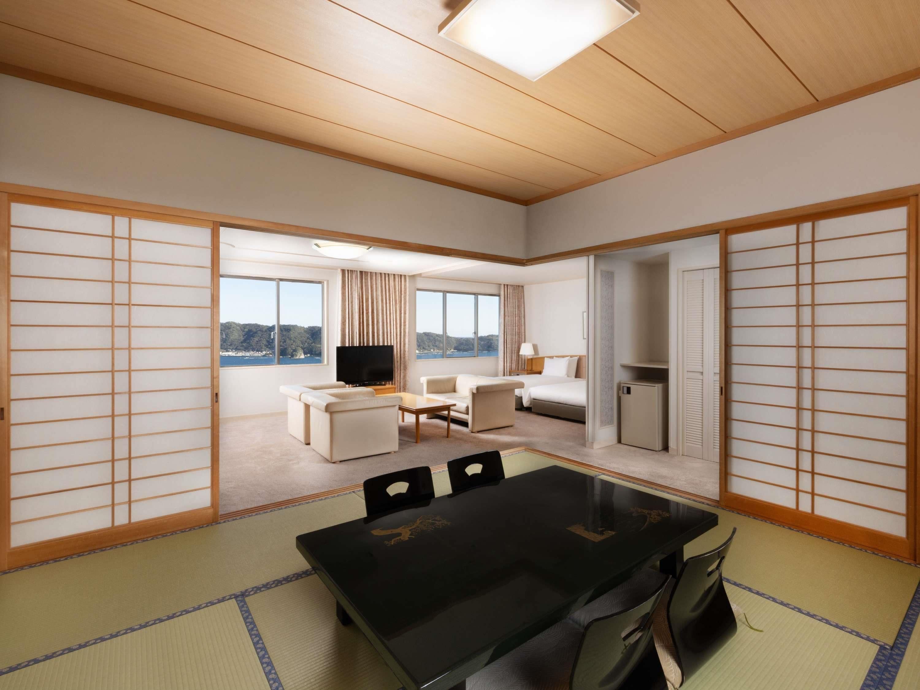 A hotel room with tatami flooring, a dining table, a TV, a bed, and a view of the sea.