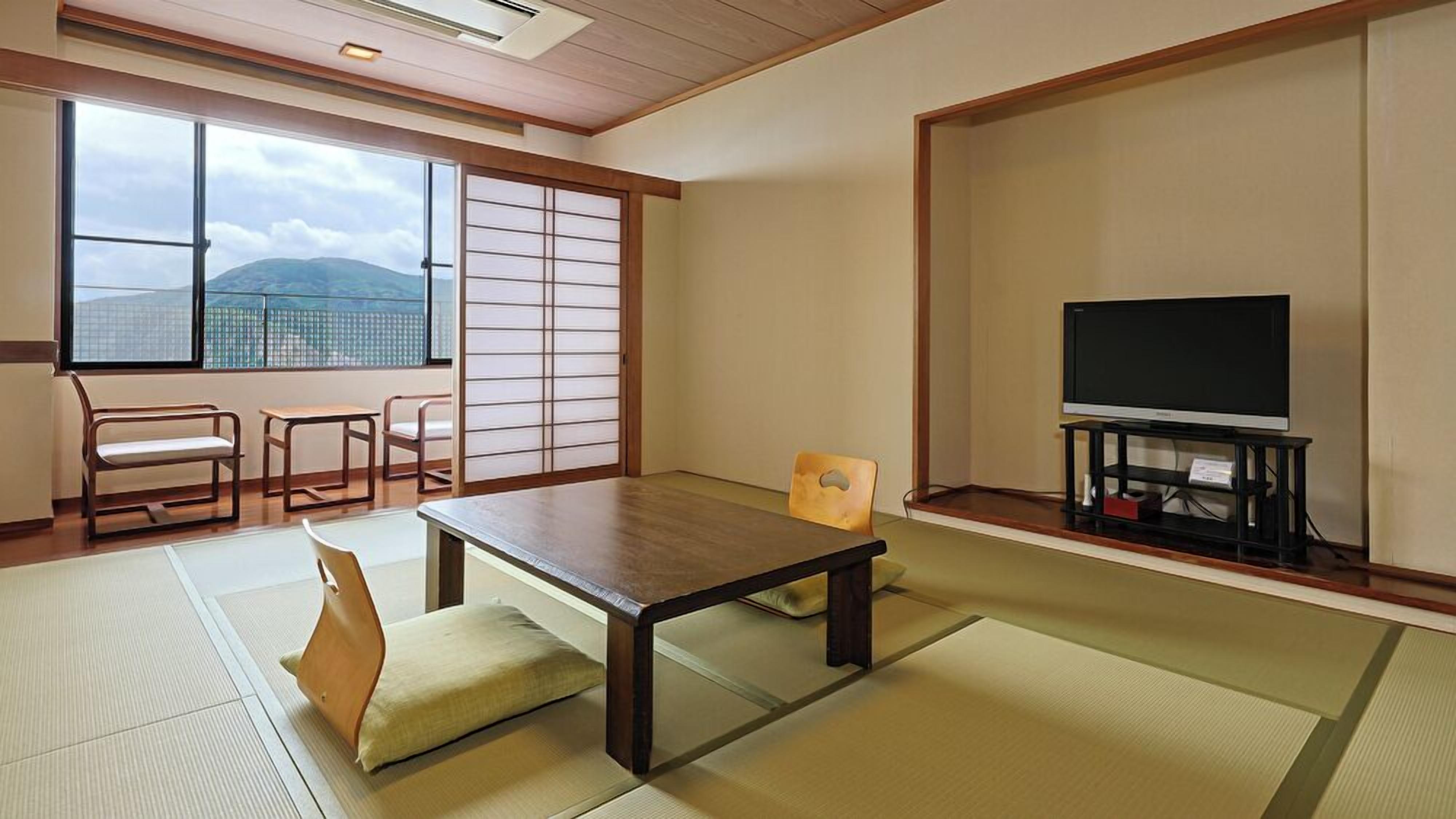 A traditional Japanese room with tatami flooring, a low table, a television on a stand, and sliding doors.