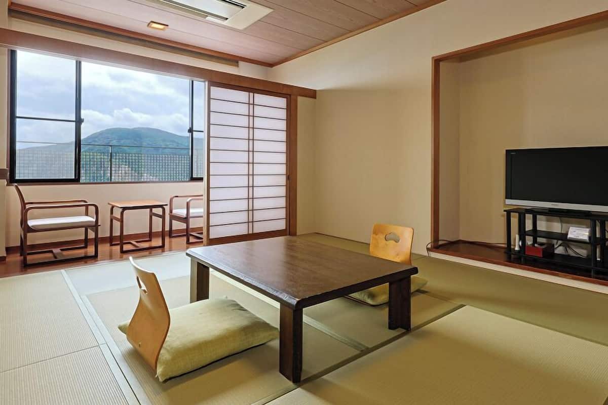 A traditional Japanese room with tatami flooring, a low table, a television on a stand, and sliding doors.