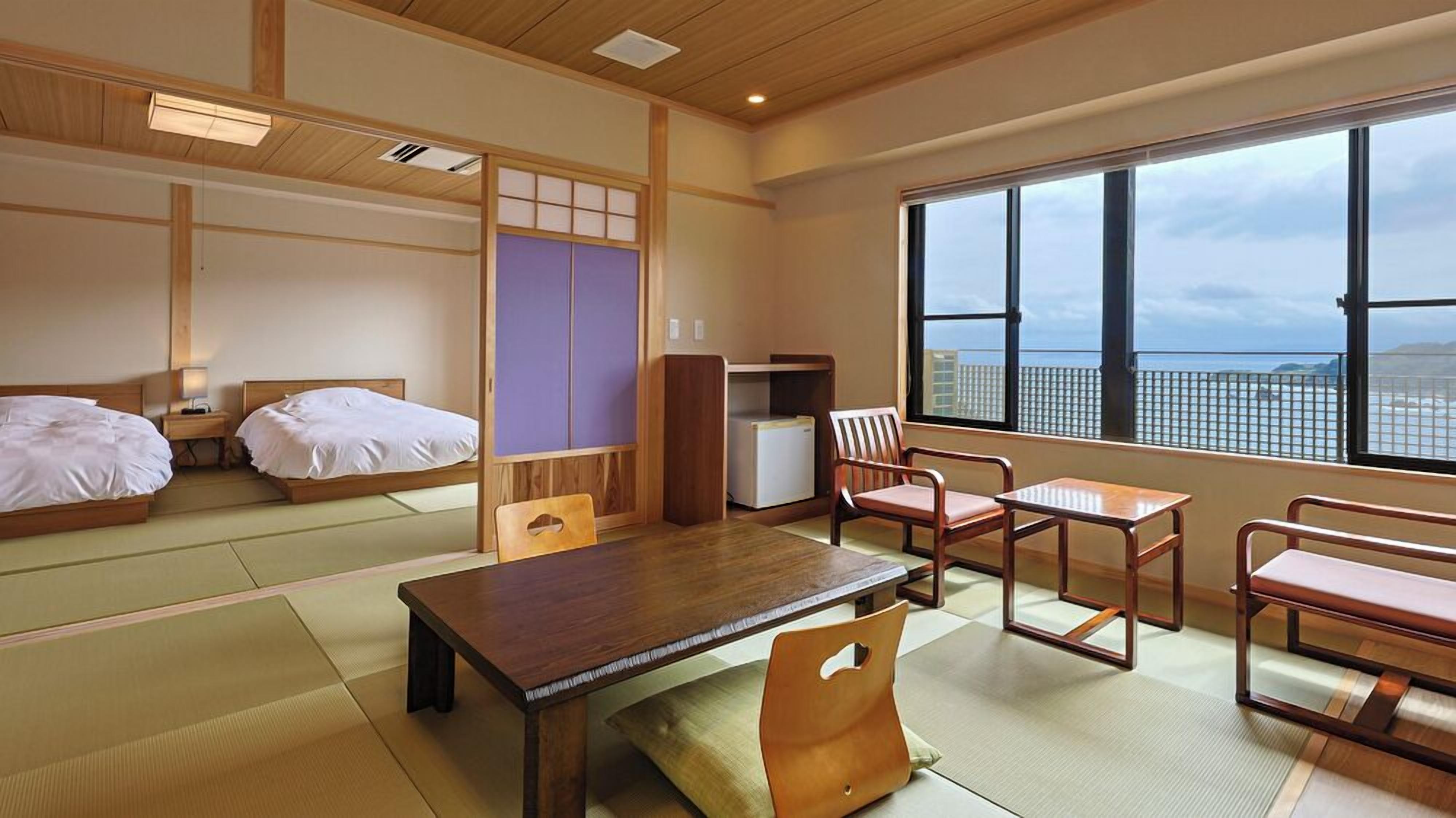 A traditional Japanese-style room with tatami flooring, a low table, and a view of the sea through large windows.