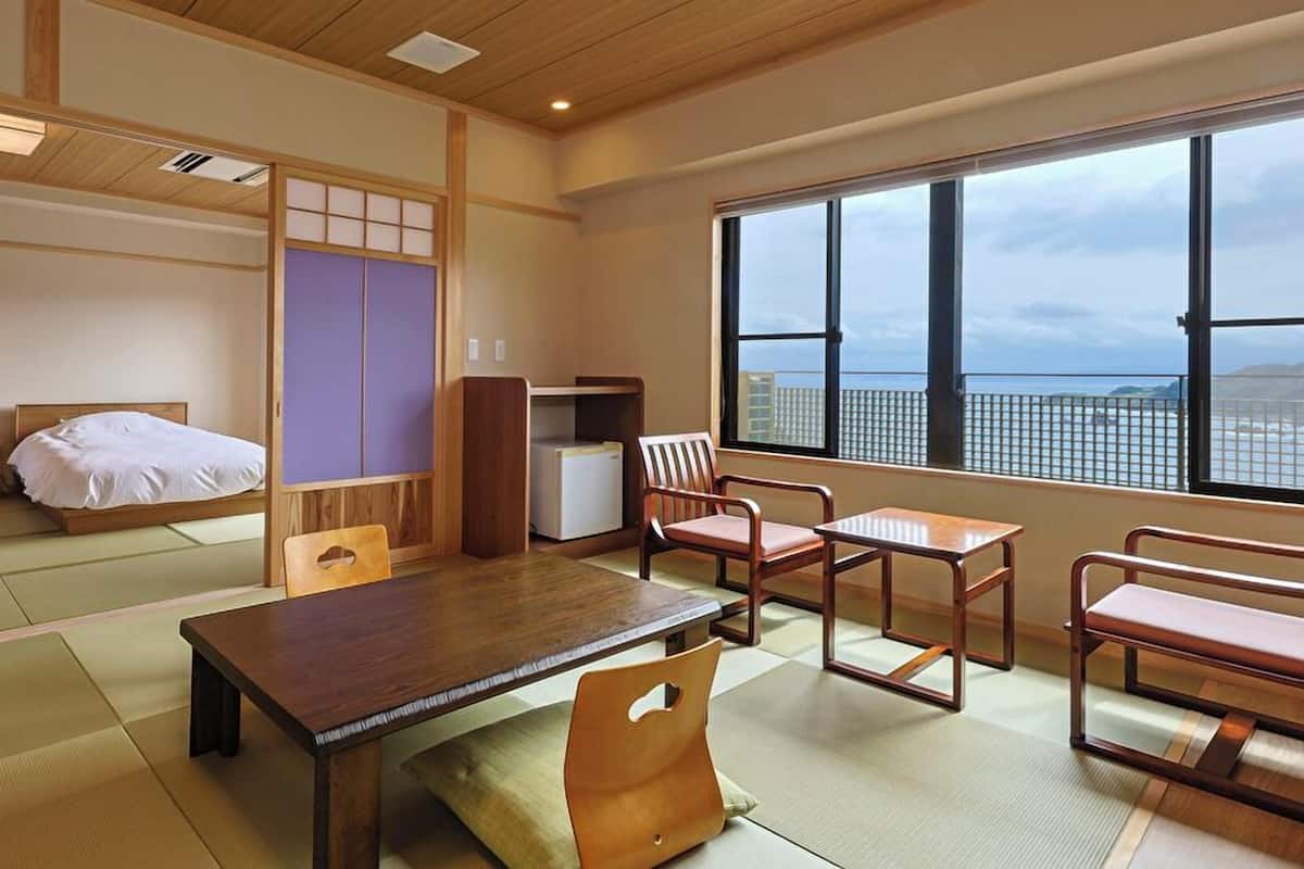 A traditional Japanese-style room with tatami flooring, a low table, and a view of the sea through large windows.