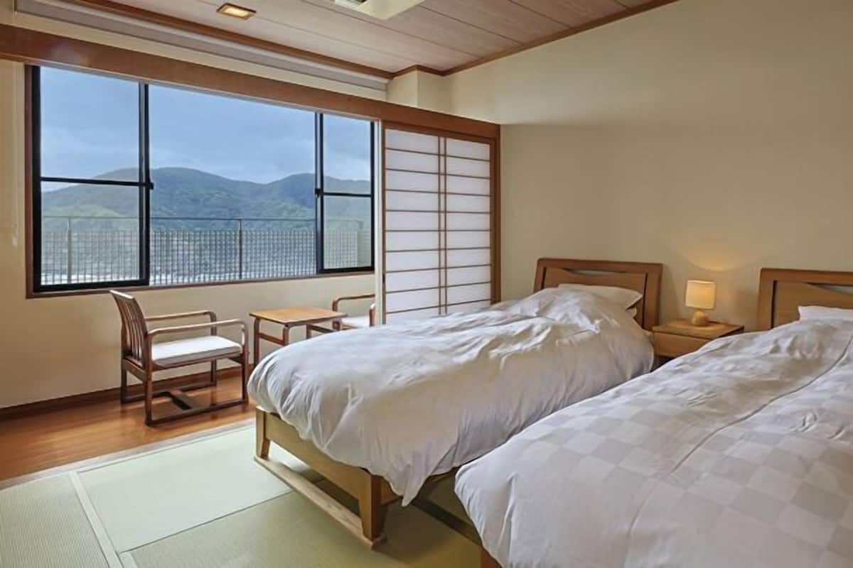 A bedroom with two beds, a desk, and a chair, with a view of mountains through large windows.