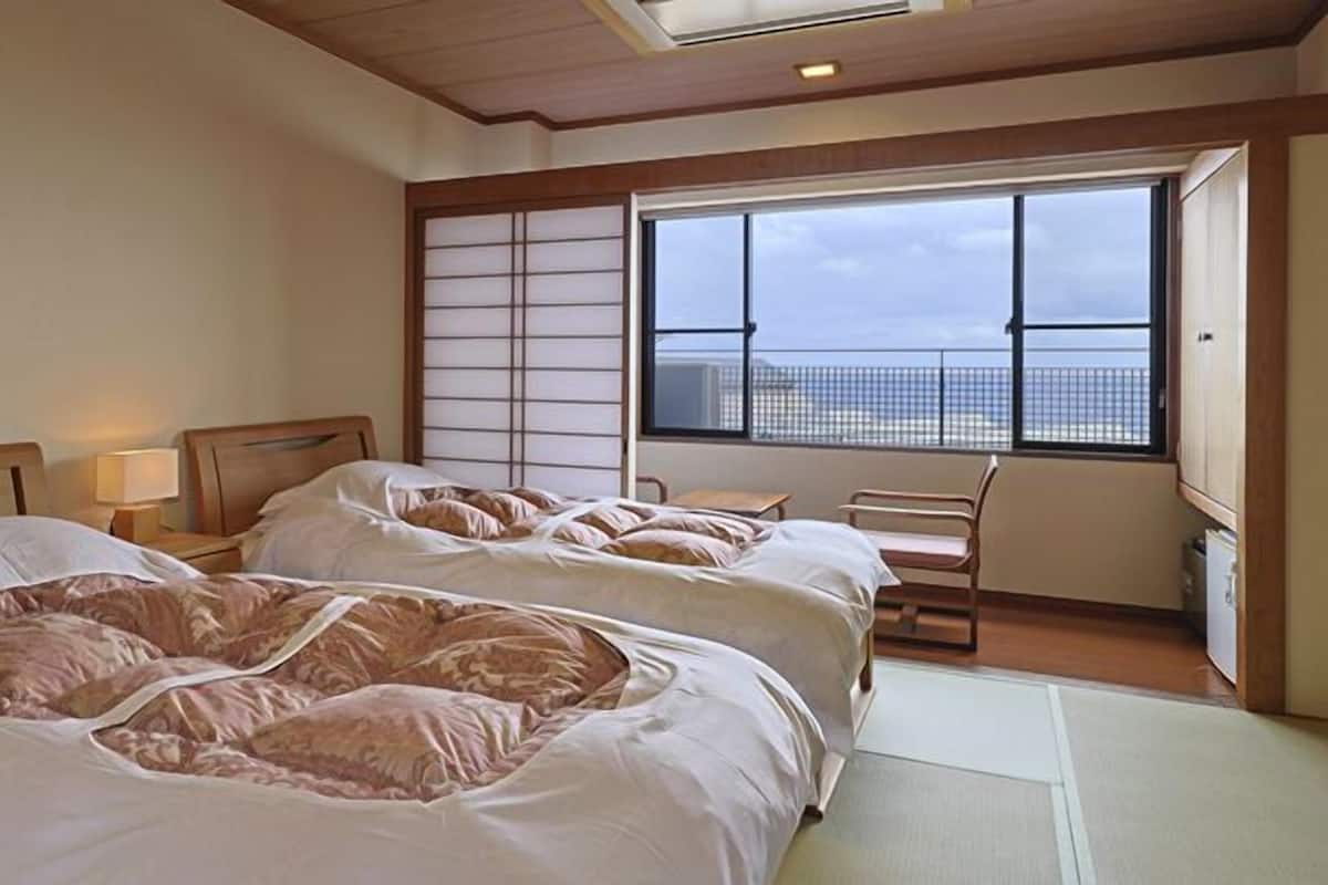 A hotel room with two beds, a large window, a view of the city, and a traditional Japanese shoji screen.