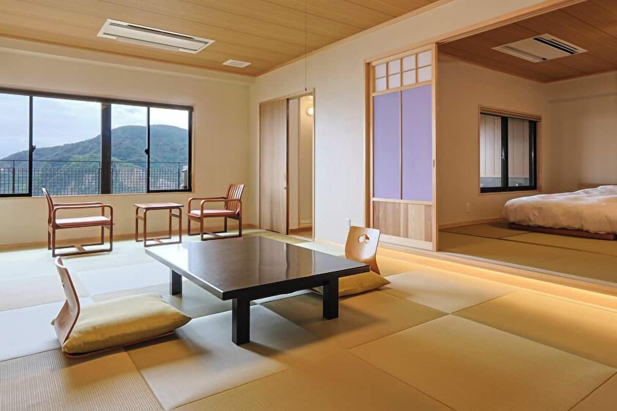 A traditional Japanese room with tatami flooring, a low table, chairs, a bed, and sliding doors.