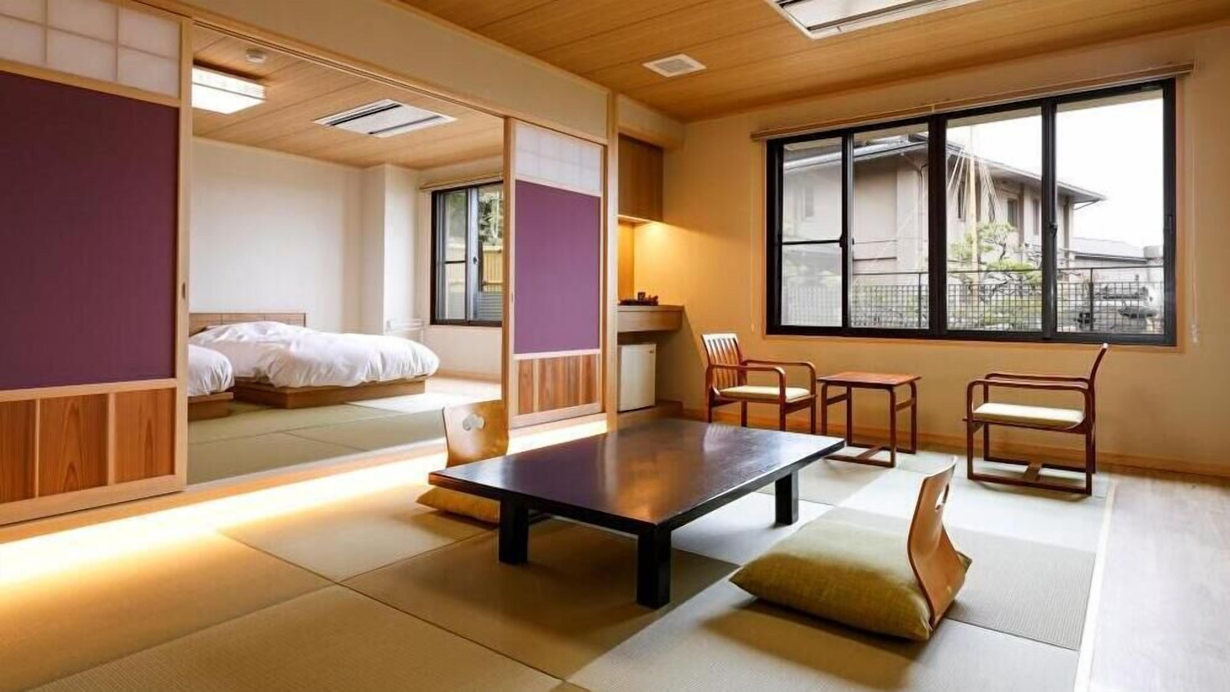 A traditional Japanese-style room with tatami flooring, a low table, and a bed with a futon.