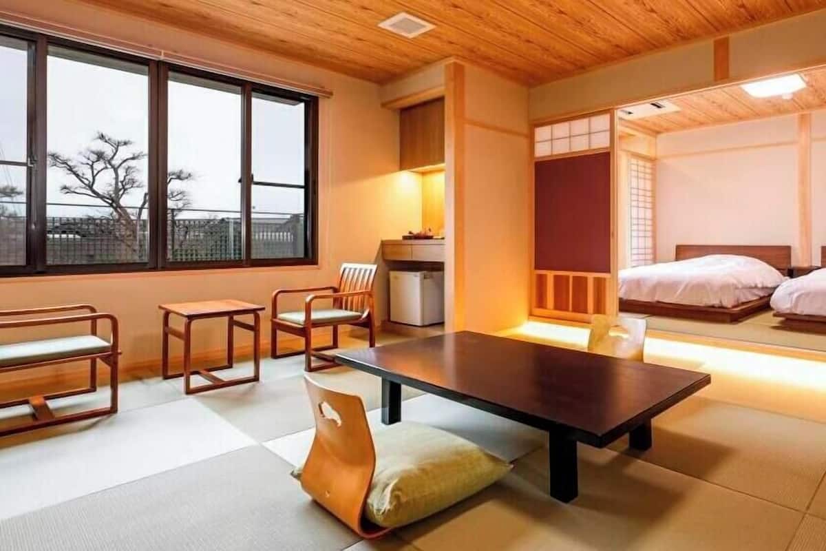 A traditional Japanese-style room with tatami flooring, a low table, a cushioned chair, a bed, and sliding doors.