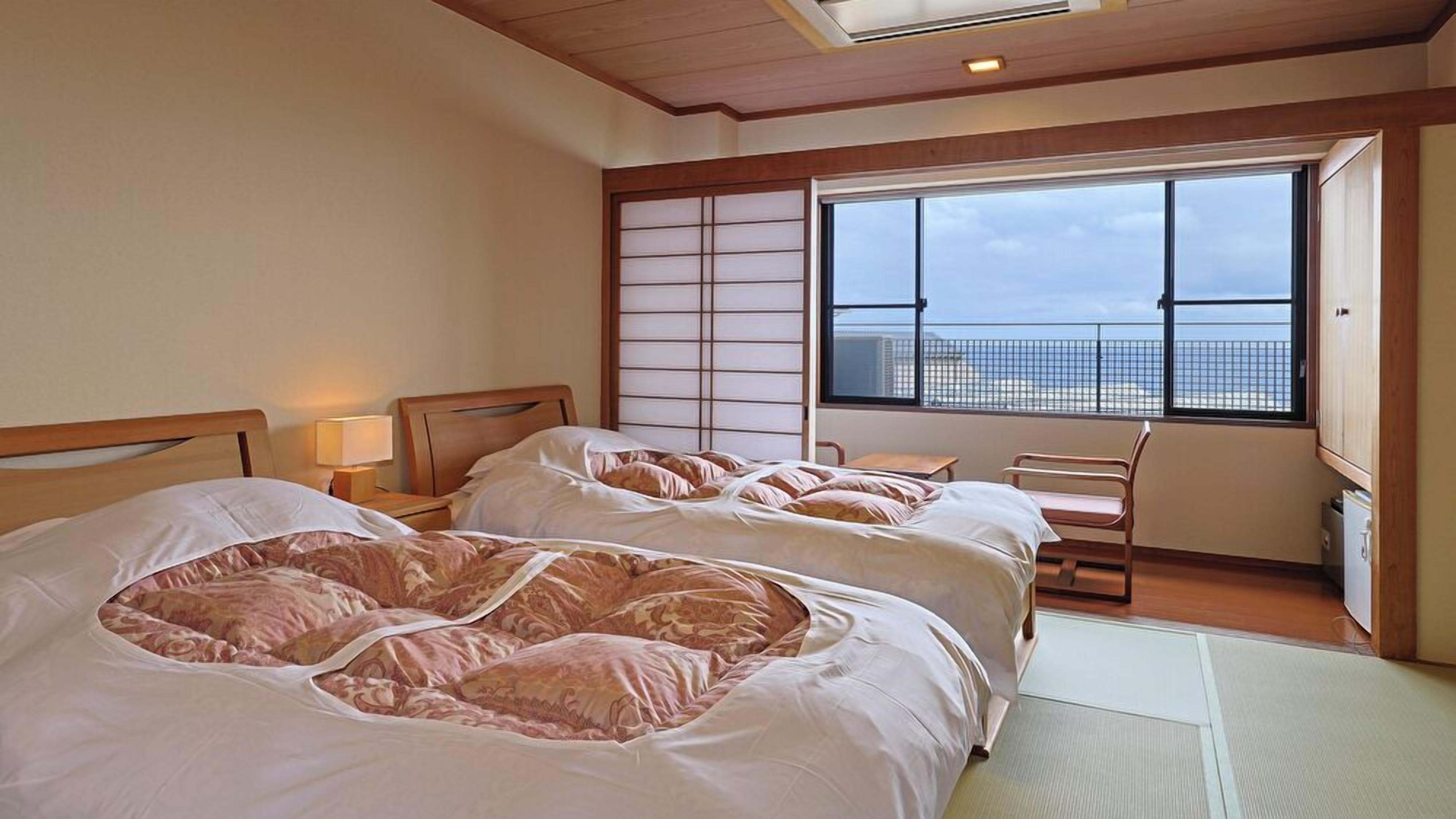 A hotel room with two beds, a view of the city, and a traditional sliding door.