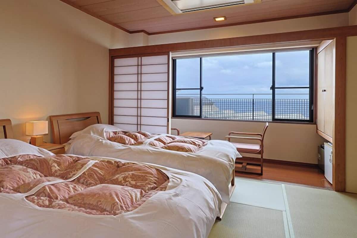 A hotel room with two beds, a view of the city, and a traditional sliding door.