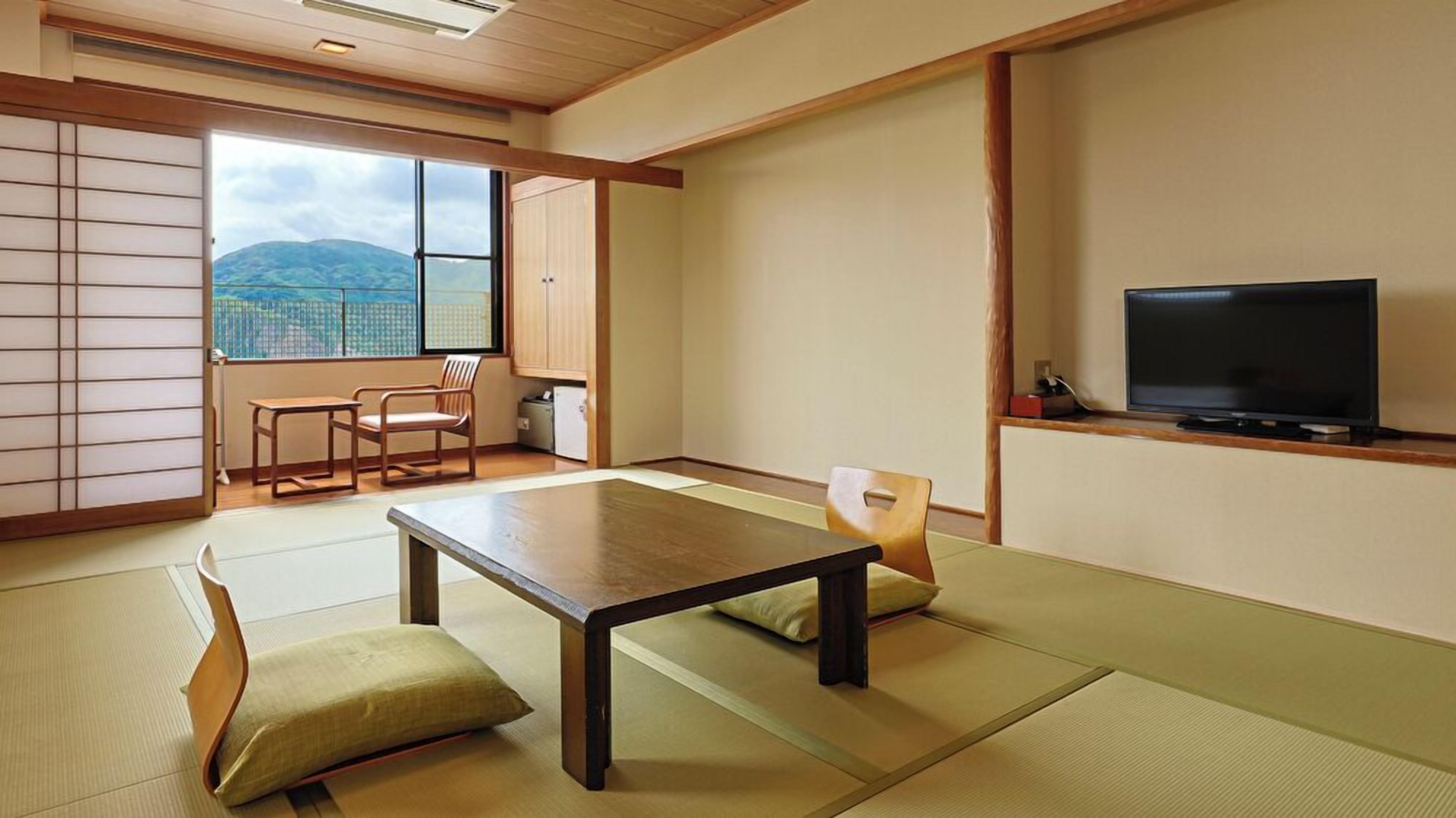 A traditional Japanese room with tatami flooring, a low table, a television, and a view of mountains.