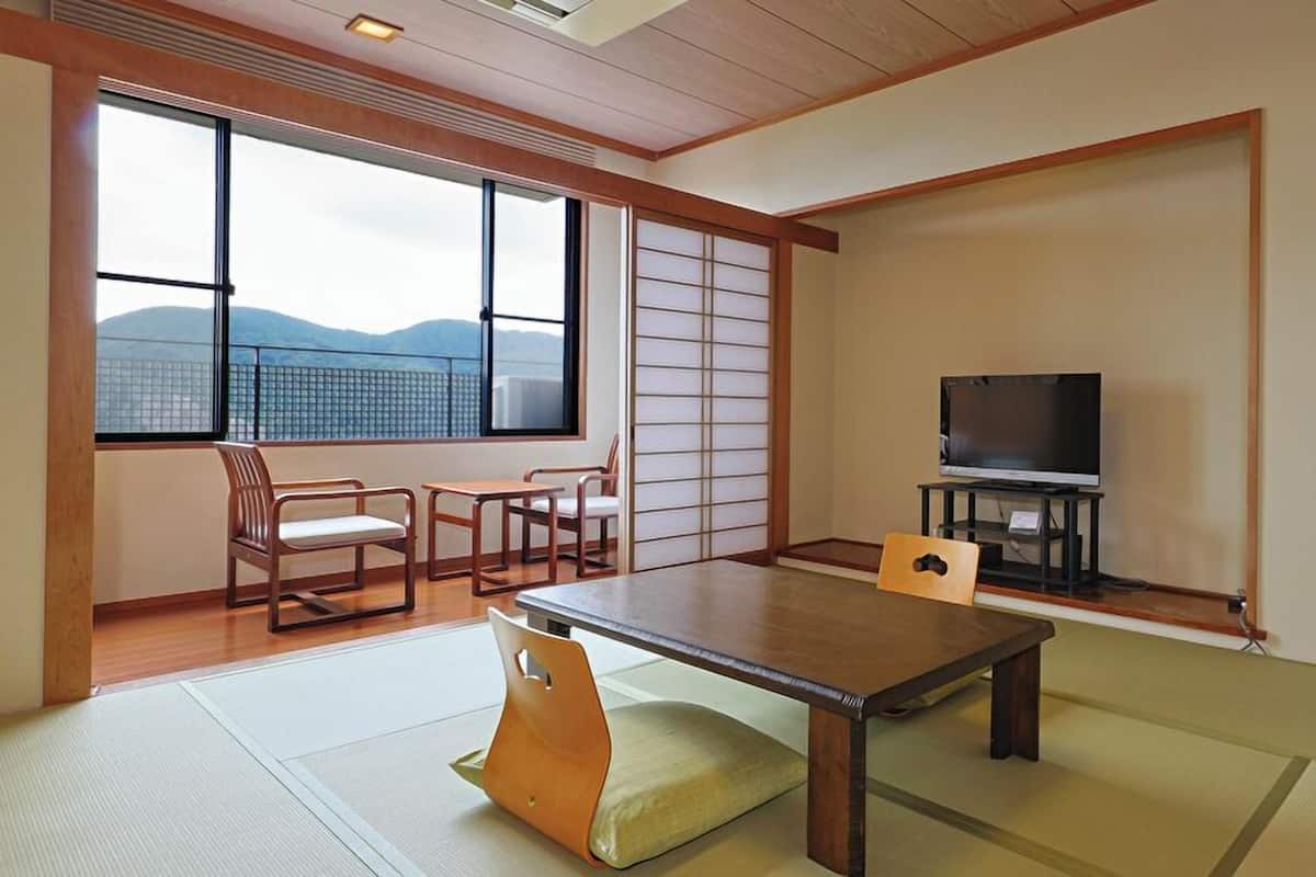 A traditional Japanese room with tatami flooring, a low table, chairs, a television, and a sliding door with shoji screens.