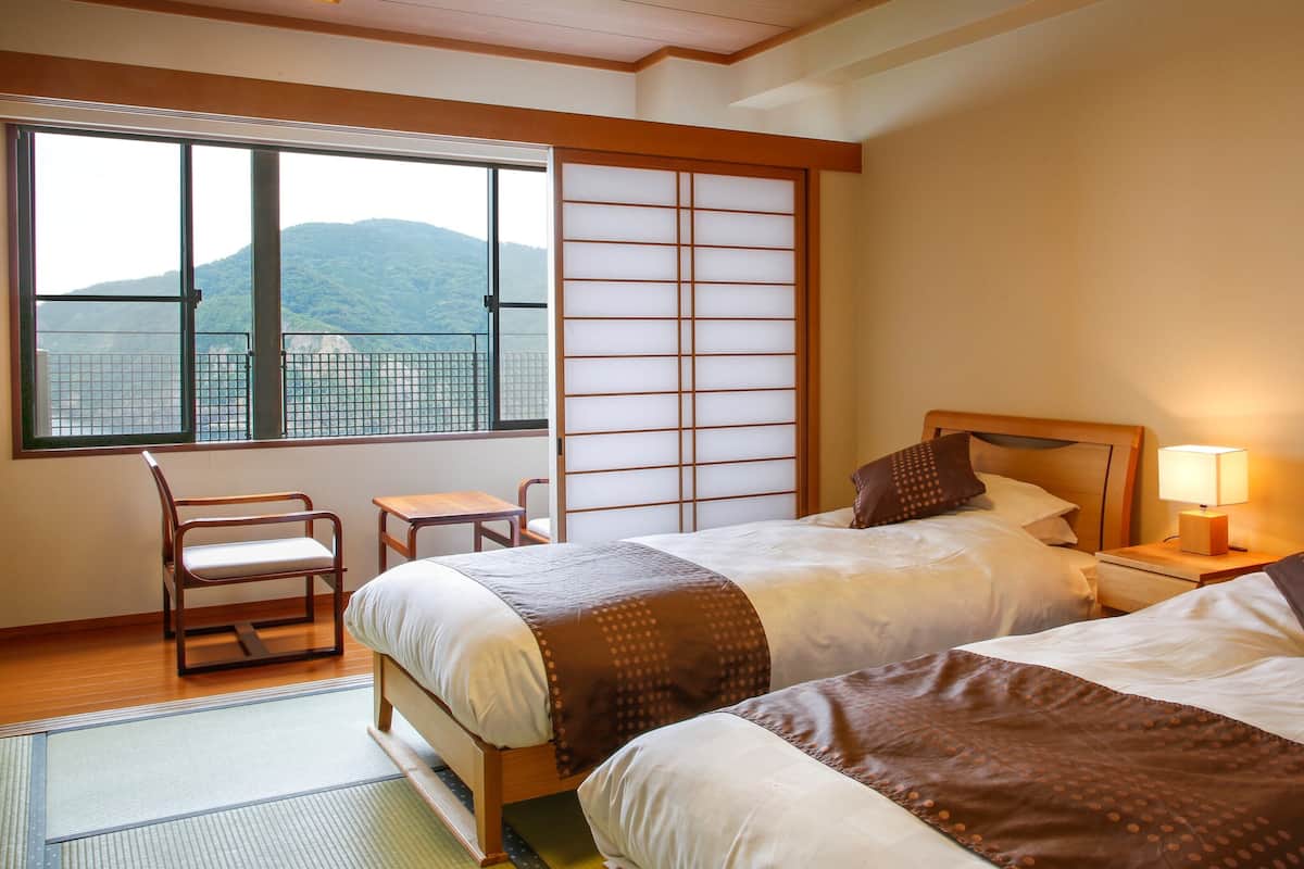 A hotel room with two beds, a chair, a small table, and a view of a mountain through a window.
