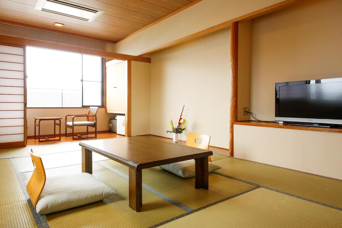 A traditional Japanese room with tatami flooring, a low table, chairs, a TV, and a sliding door.
